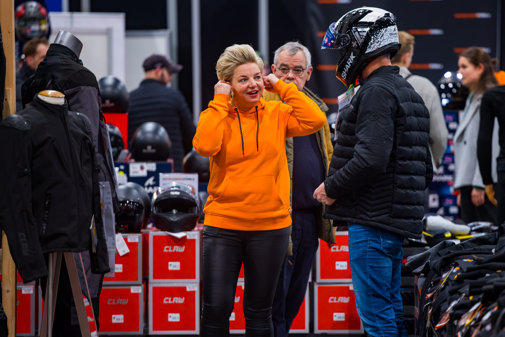 Man past helm terwijl vrouw in een oranje hoodie advies geeft bij de MotorkledingStore stand