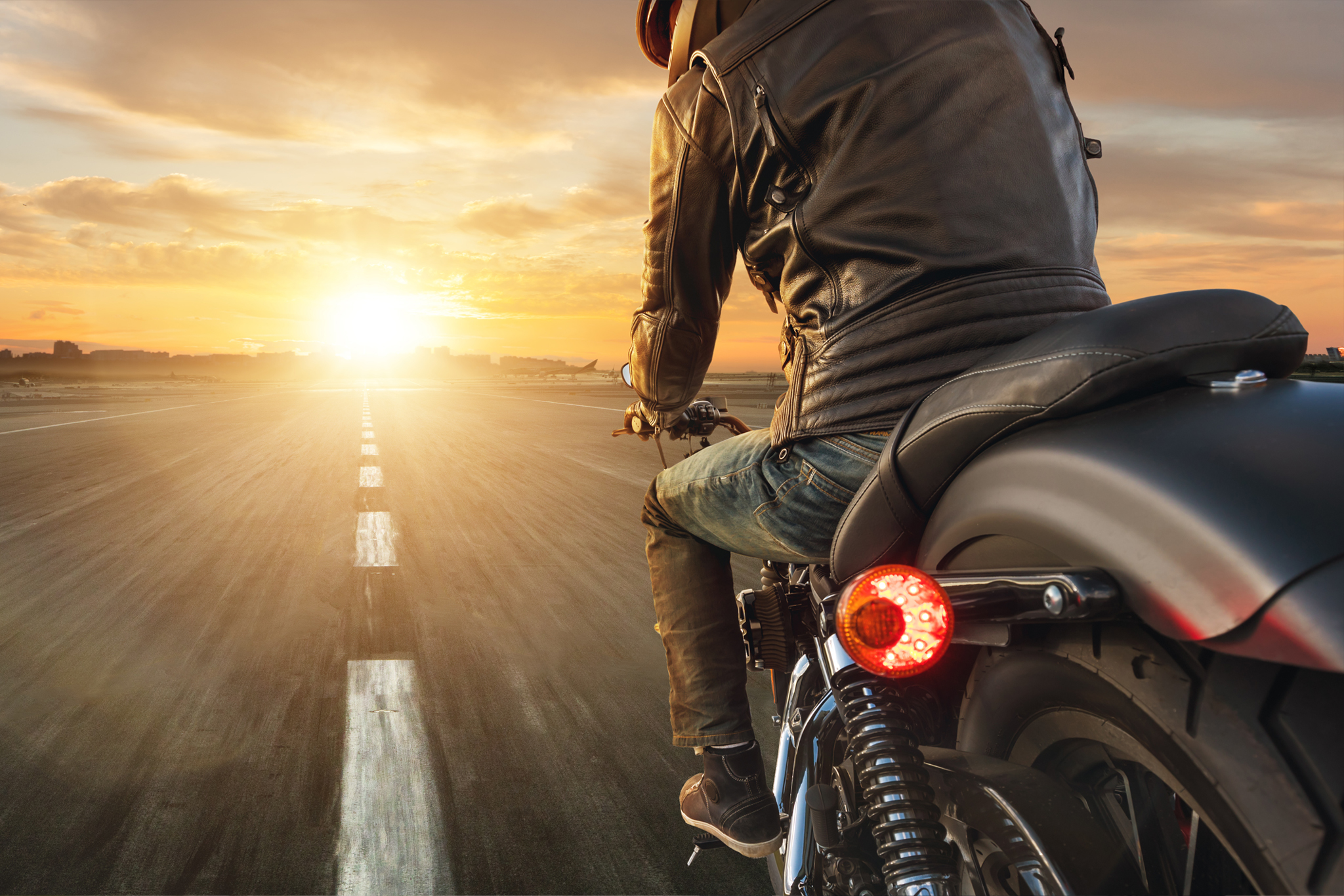 Motorrijder in een leren jas rijdt een klassieke motor richting de zonsondergang op een open weg