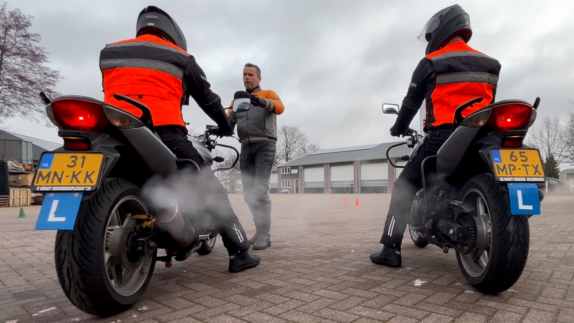 Rijinstructeur geeft motorrijles aan twee leerlingen op het oefenterrein van een motorrijschool