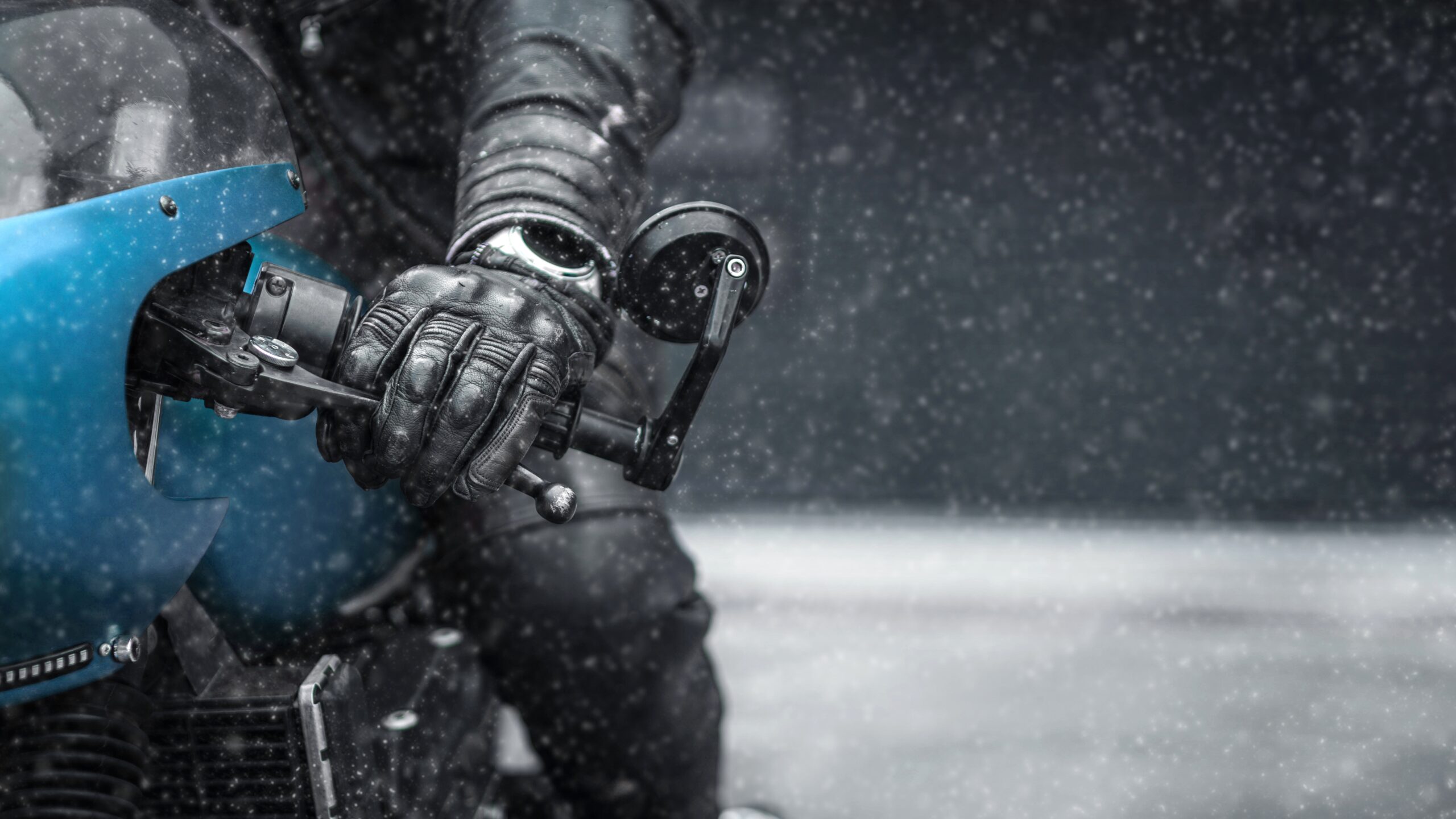 Close-up of a motorcyclist in winter conditions, with leather gloves and falling snow